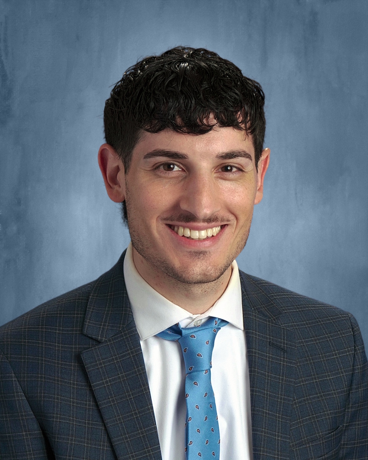 Photo of man wearing suit with light blue tie, against a blue background